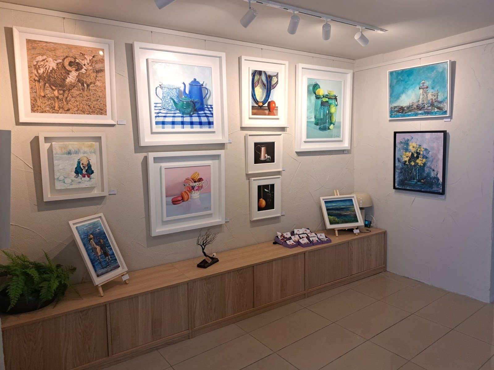 A corner of the gallery with framed original paintings hung above an oak display unit